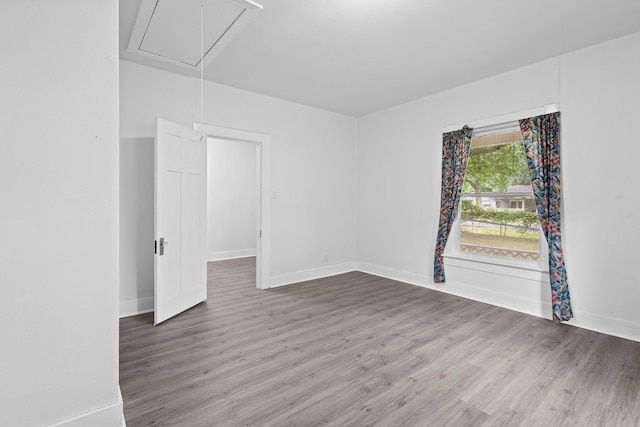 unfurnished room featuring baseboards, wood finished floors, and attic access