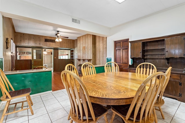 tiled dining room with ceiling fan, crown molding, and wood walls