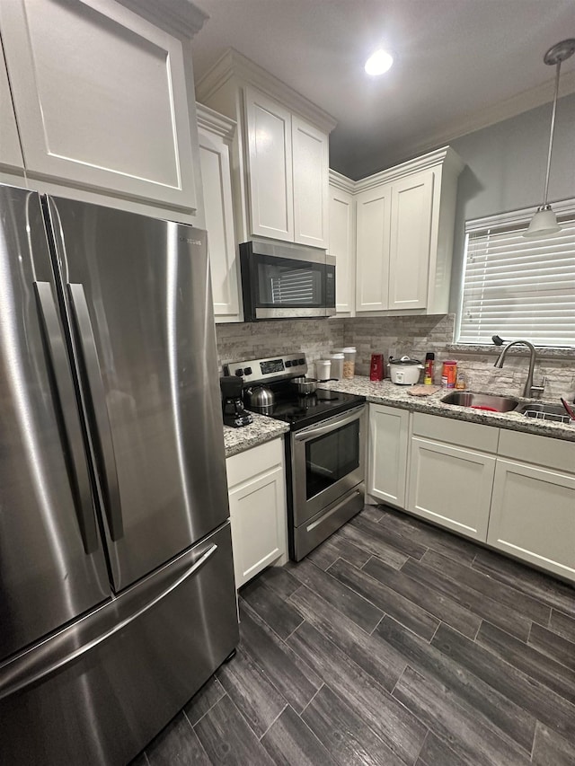 kitchen with light stone countertops, appliances with stainless steel finishes, sink, white cabinetry, and hanging light fixtures