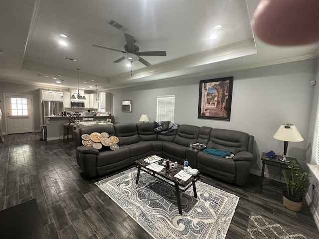 living room with a tray ceiling, ceiling fan, and dark wood-type flooring