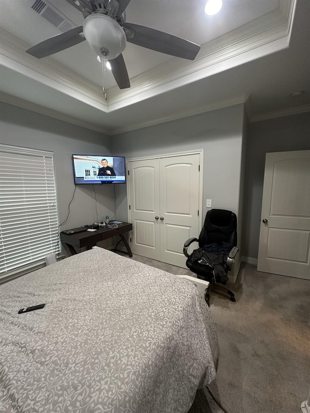 carpeted bedroom featuring a closet, a tray ceiling, ceiling fan, and ornamental molding