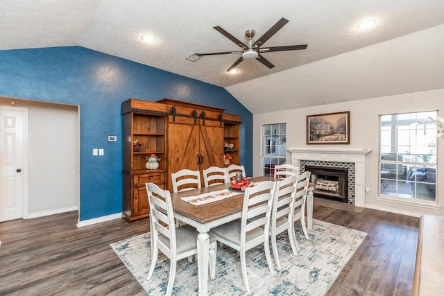 dining space featuring ceiling fan, dark hardwood / wood-style floors, a textured ceiling, vaulted ceiling, and a tiled fireplace