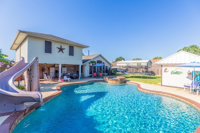 view of swimming pool with a trampoline, pool water feature, a water slide, a patio area, and an in ground hot tub