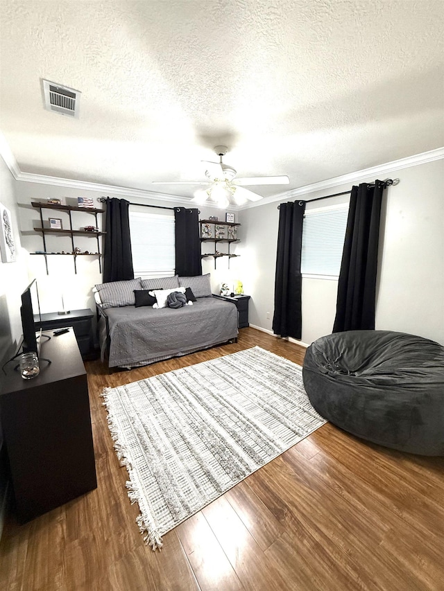 bedroom with crown molding, wood finished floors, a textured ceiling, and visible vents