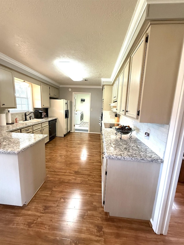 kitchen with a sink, a textured ceiling, white fridge with ice dispenser, ornamental molding, and washer and clothes dryer