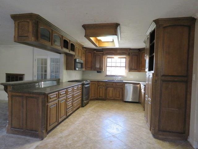 kitchen featuring sink, a skylight, light tile patterned floors, kitchen peninsula, and stainless steel appliances