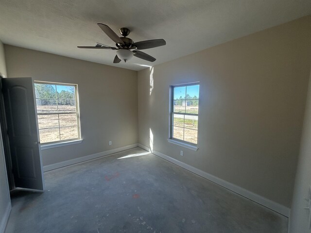 empty room featuring plenty of natural light, concrete floors, baseboards, and ceiling fan