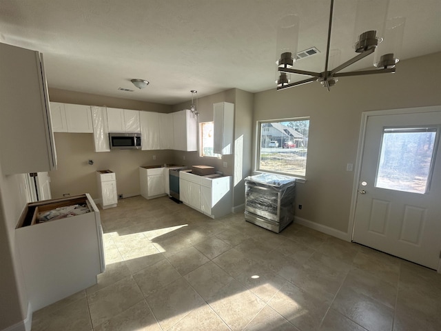 kitchen with stainless steel microwave, hanging light fixtures, visible vents, white cabinetry, and baseboards