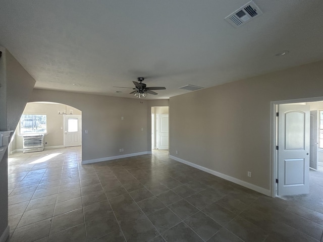 empty room featuring arched walkways, baseboards, visible vents, and a ceiling fan