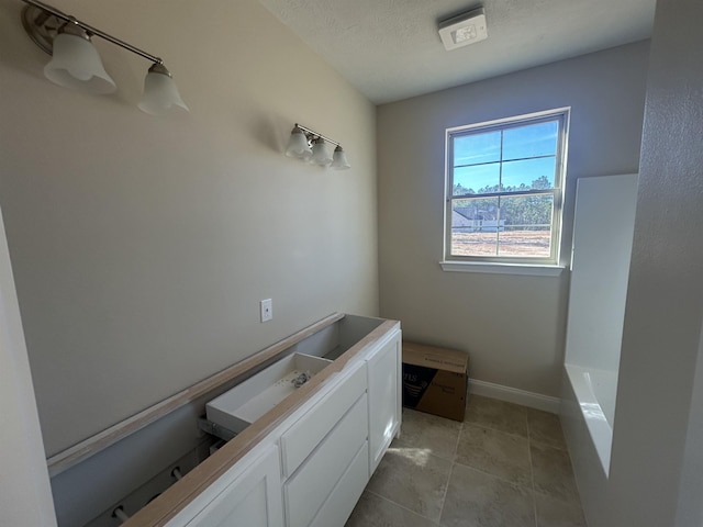 full bath featuring a bath, baseboards, a textured ceiling, and tile patterned floors