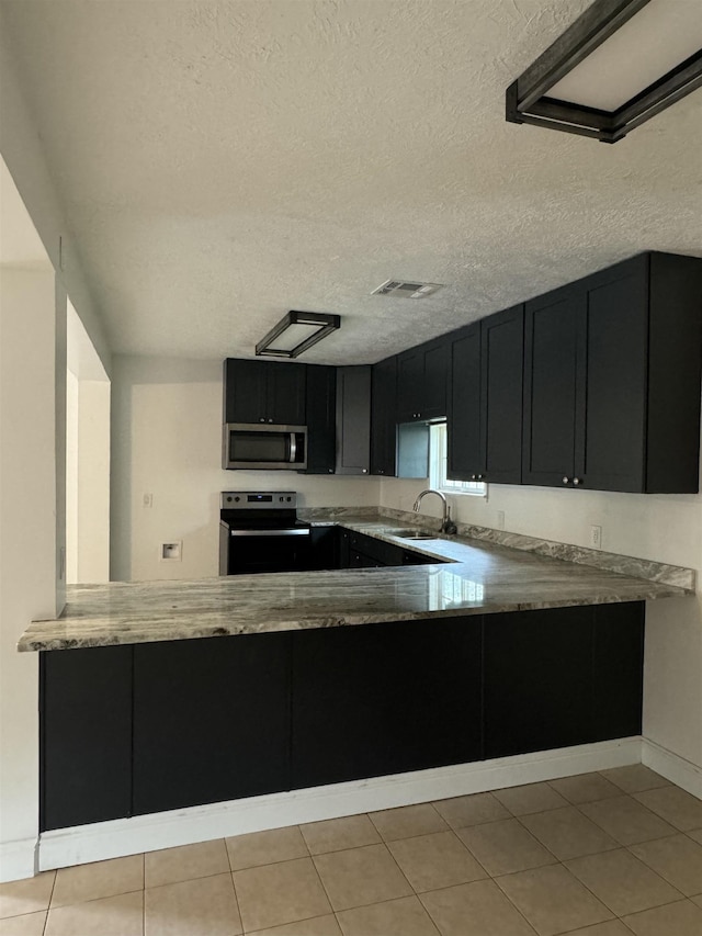 kitchen featuring sink, kitchen peninsula, a textured ceiling, light tile patterned flooring, and appliances with stainless steel finishes