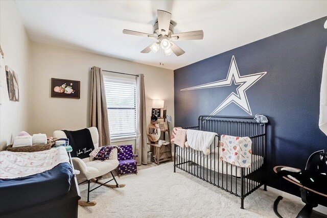 carpeted bedroom featuring ceiling fan and a crib