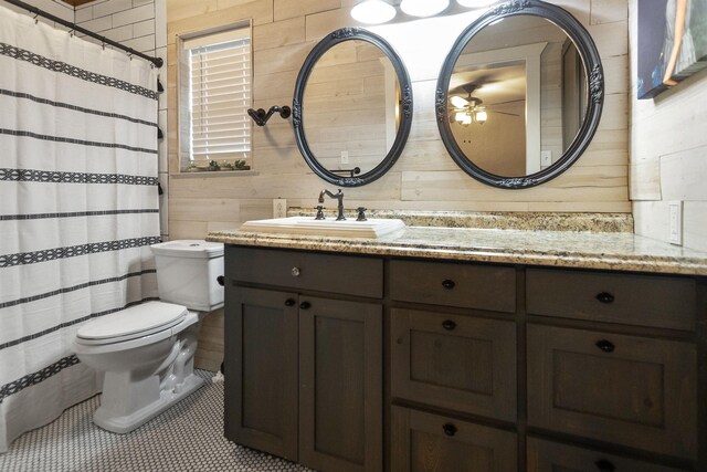 bathroom with tile patterned floors, vanity, ceiling fan, toilet, and wood walls