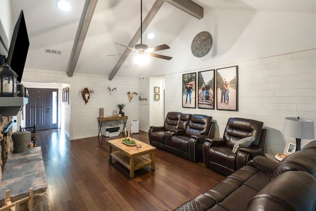 living room featuring ceiling fan, dark wood-type flooring, vaulted ceiling with beams, a stone fireplace, and wood walls