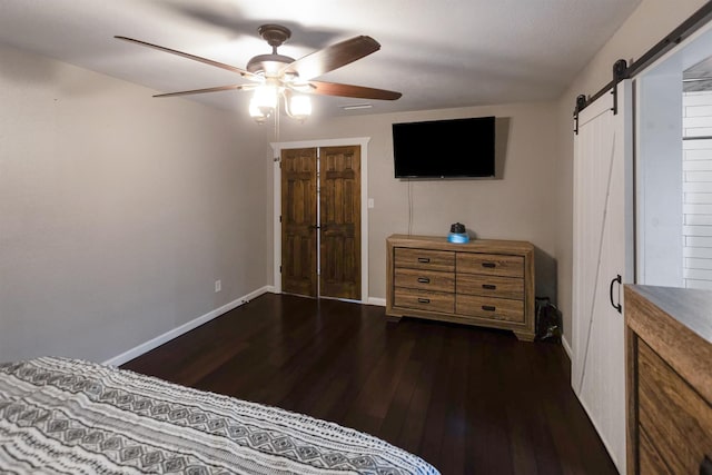 bedroom with ceiling fan, a barn door, dark wood-type flooring, and a closet