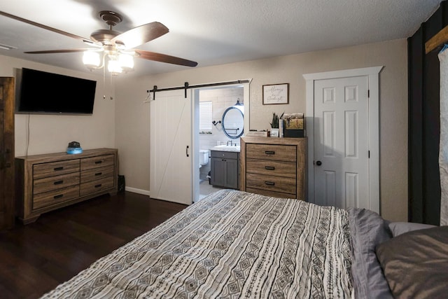 bedroom featuring ensuite bath, a textured ceiling, ceiling fan, dark wood-type flooring, and a barn door