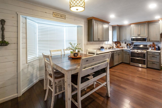 kitchen featuring dark hardwood / wood-style flooring, sink, stainless steel appliances, and wood walls