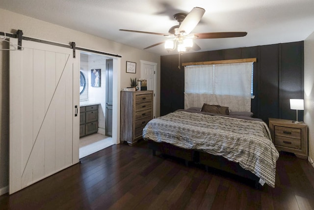 bedroom with ceiling fan, a barn door, dark wood-type flooring, and connected bathroom