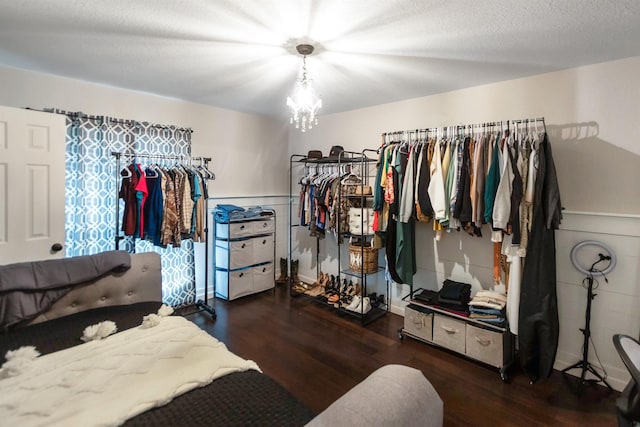 walk in closet with dark wood-type flooring and an inviting chandelier