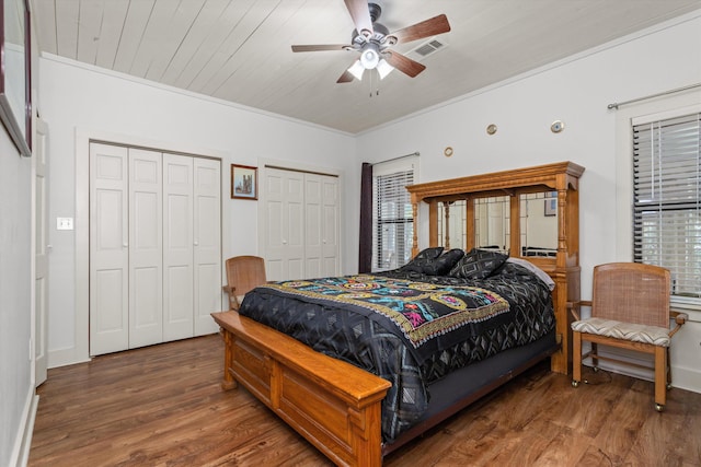 bedroom with wooden ceiling, two closets, ceiling fan, ornamental molding, and dark hardwood / wood-style flooring