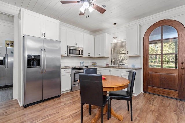 kitchen with appliances with stainless steel finishes, decorative light fixtures, white cabinetry, and light hardwood / wood-style flooring