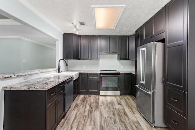 12795 Tanoak Ln, Beaumont, TX 77713 - kitchen featuring appliances with stainless steel finishes, a peninsula, light wood-style flooring, a textured ceiling, and light stone counters