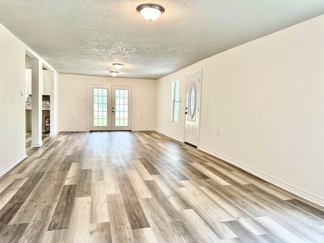 unfurnished living room with french doors, a textured ceiling, and light hardwood / wood-style flooring