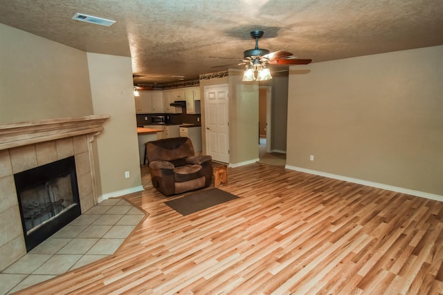 unfurnished living room featuring baseboards, a tile fireplace, visible vents, and light wood-style floors