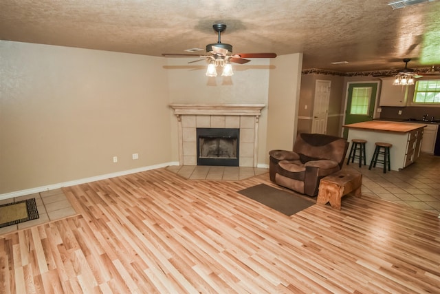 unfurnished living room featuring a ceiling fan, a tile fireplace, a textured ceiling, and light wood finished floors