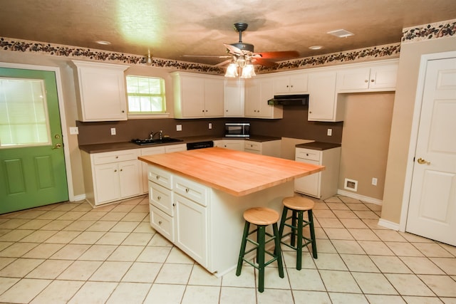 kitchen with a breakfast bar area, white cabinets, light tile patterned flooring, ceiling fan, and butcher block countertops