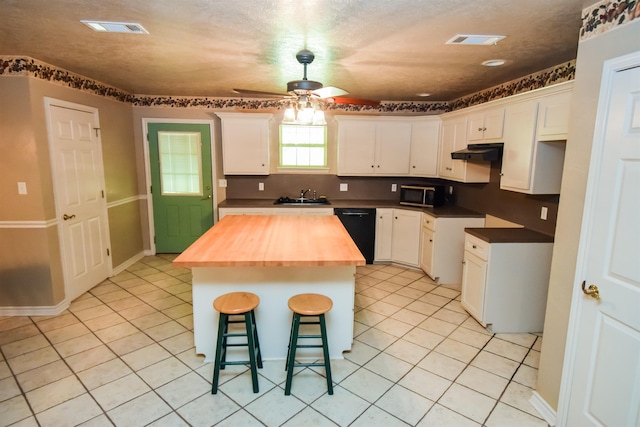 kitchen featuring light tile patterned floors, wood counters, visible vents, a kitchen breakfast bar, and black dishwasher