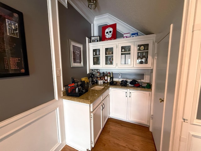 bar featuring white cabinetry, sink, crown molding, hardwood / wood-style floors, and dark stone counters