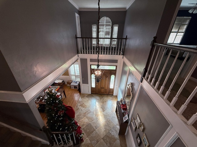 foyer featuring crown molding, plenty of natural light, a towering ceiling, and a chandelier