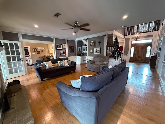 living room with ceiling fan with notable chandelier, light wood-type flooring, and ornamental molding