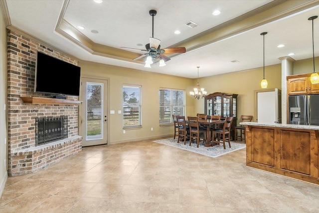 kitchen featuring a tray ceiling, ornamental molding, a brick fireplace, stainless steel fridge with ice dispenser, and ceiling fan with notable chandelier