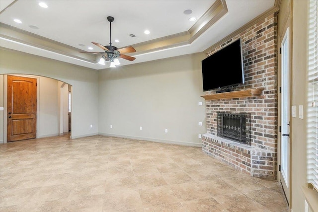 unfurnished living room featuring crown molding, ceiling fan, a fireplace, and a raised ceiling