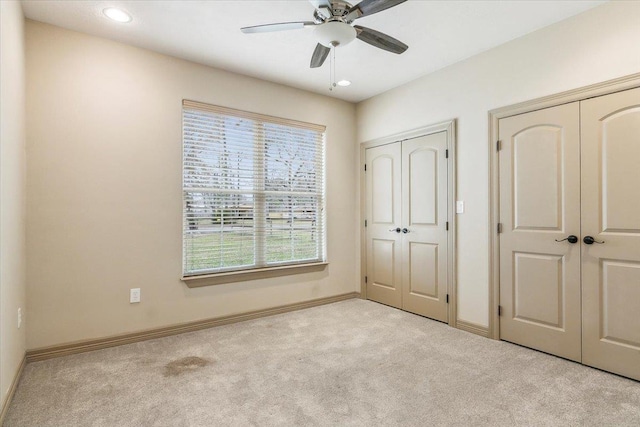 unfurnished bedroom with light carpet, ceiling fan, and multiple closets