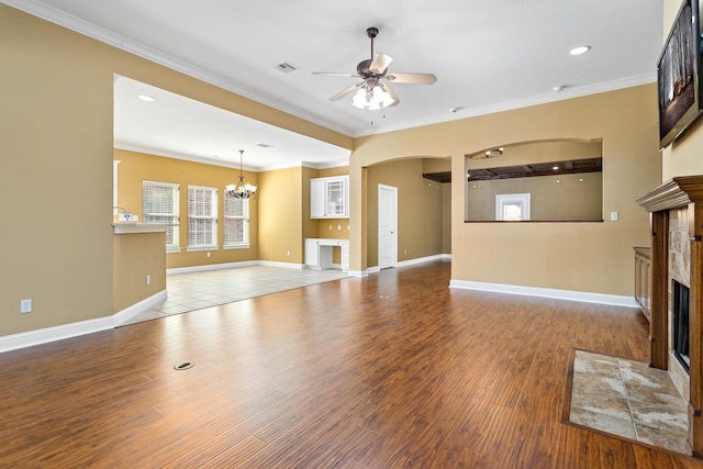 unfurnished living room featuring a tiled fireplace, crown molding, wood-type flooring, and ceiling fan with notable chandelier