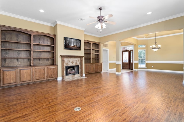 unfurnished living room with a high end fireplace, ceiling fan with notable chandelier, built in shelves, ornamental molding, and wood-type flooring