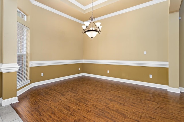 empty room with a raised ceiling, hardwood / wood-style flooring, an inviting chandelier, and ornamental molding