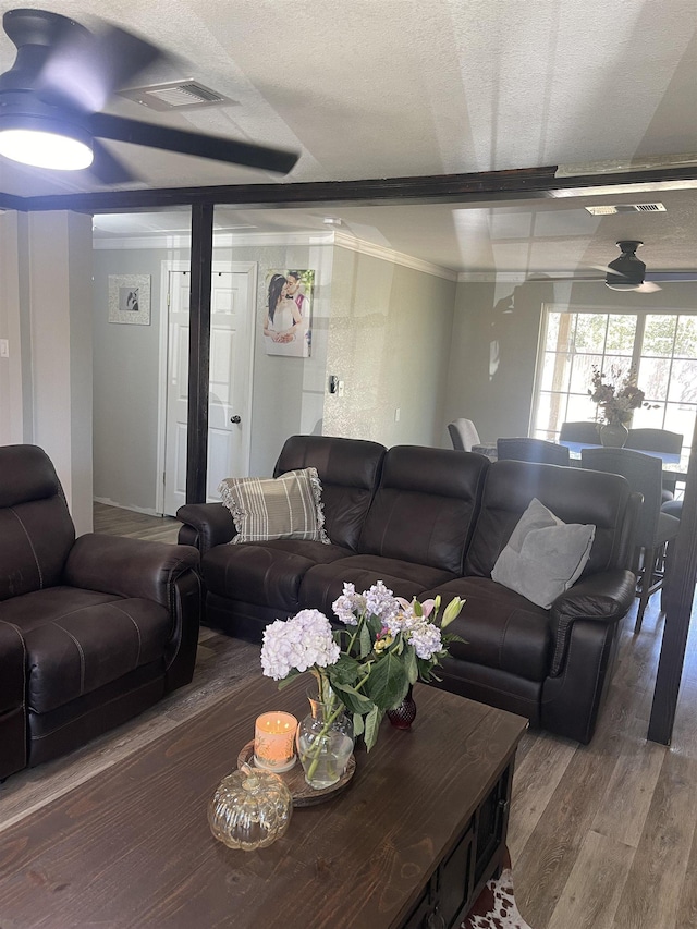 living room featuring hardwood / wood-style flooring, ceiling fan, ornamental molding, a textured ceiling, and beamed ceiling