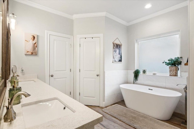 bathroom with ornamental molding, vanity, wood-type flooring, tile walls, and a bathing tub