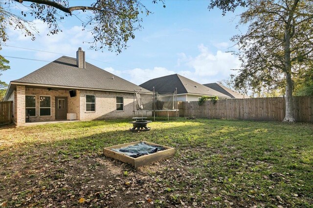 back of house with a trampoline and a yard