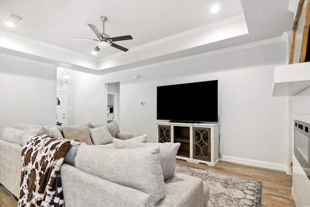 living room with a tray ceiling, crown molding, ceiling fan, and light wood-type flooring