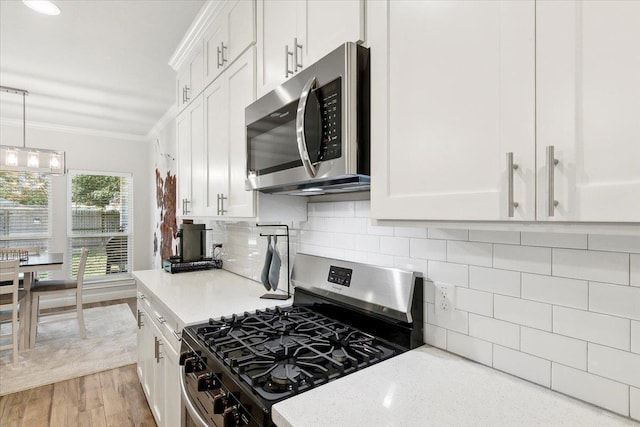 kitchen featuring appliances with stainless steel finishes, crown molding, pendant lighting, light hardwood / wood-style flooring, and white cabinetry