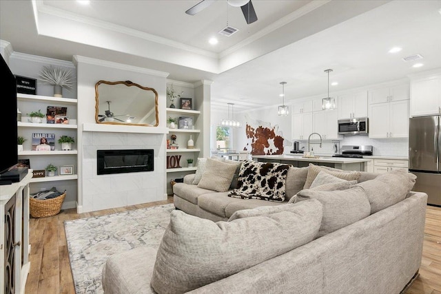 living room featuring a raised ceiling, light hardwood / wood-style flooring, and a tiled fireplace