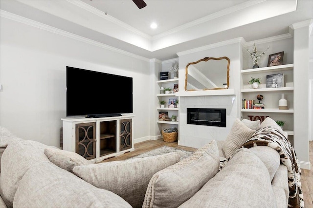 living room featuring ceiling fan, light hardwood / wood-style flooring, a tray ceiling, a tiled fireplace, and ornamental molding