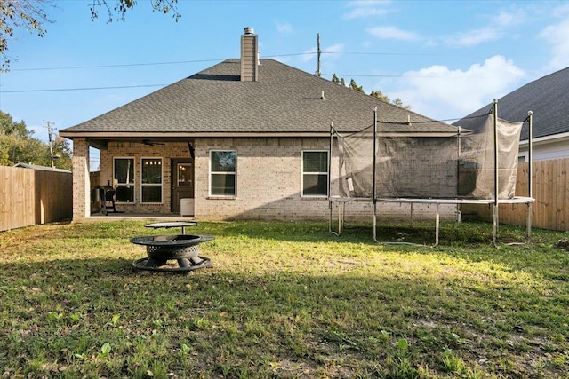 rear view of property featuring a lawn, ceiling fan, and a trampoline