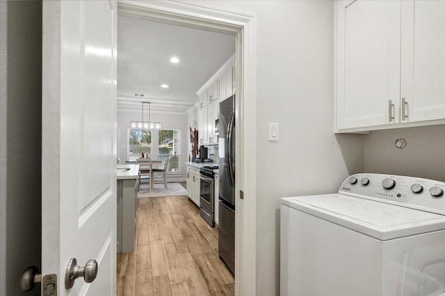 clothes washing area with cabinets, washer / dryer, and light hardwood / wood-style flooring