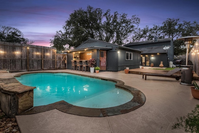 pool at dusk with a patio area, a fenced backyard, outdoor dry bar, and a fenced in pool